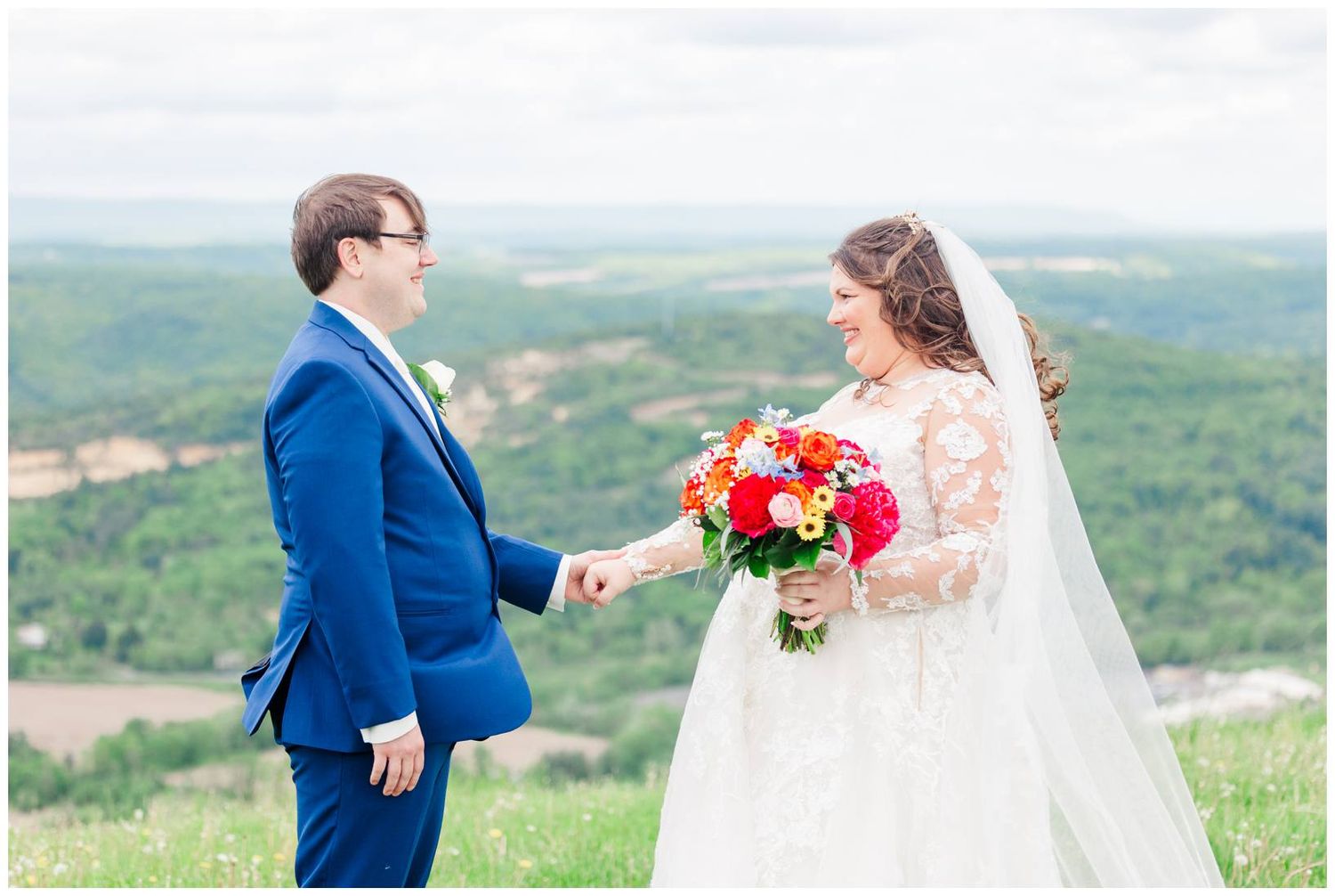 A bride and groom share a moment together on a mountaintop overlooking a scenic valley landscape.
