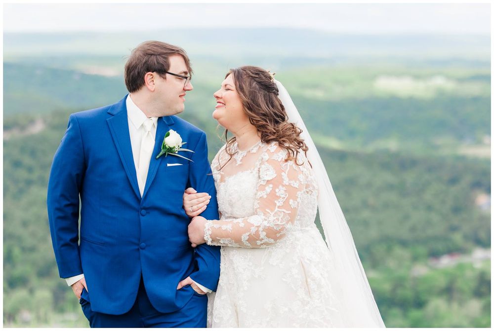 Two newlyweds share a joyful moment outdoors in wedding attire against a scenic mountain landscape background.