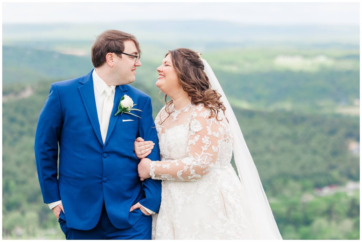 Two newlyweds share a joyful moment outdoors in wedding attire against a scenic mountain landscape background.