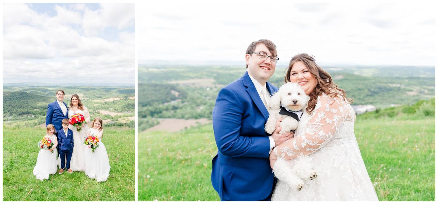 A couple poses on a scenic hillside with a white dog during their wedding celebration on a bright spring day.