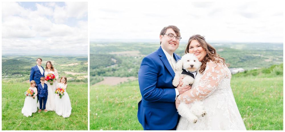 A couple poses on a scenic hillside with a white dog during their wedding celebration on a bright spring day.