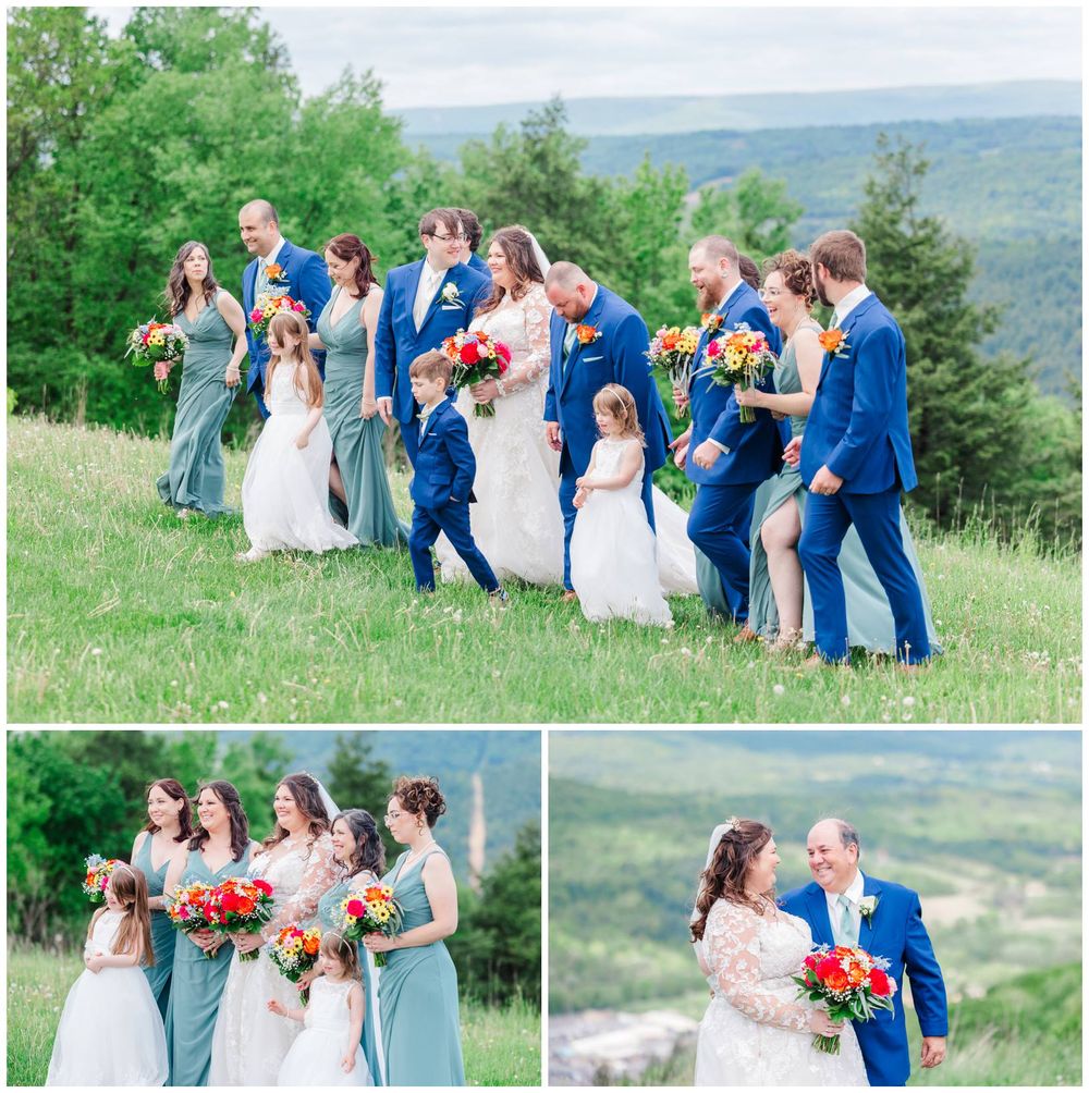 Wedding party in blue and gray attire poses together on a scenic hilltop overlooking rolling landscapes.