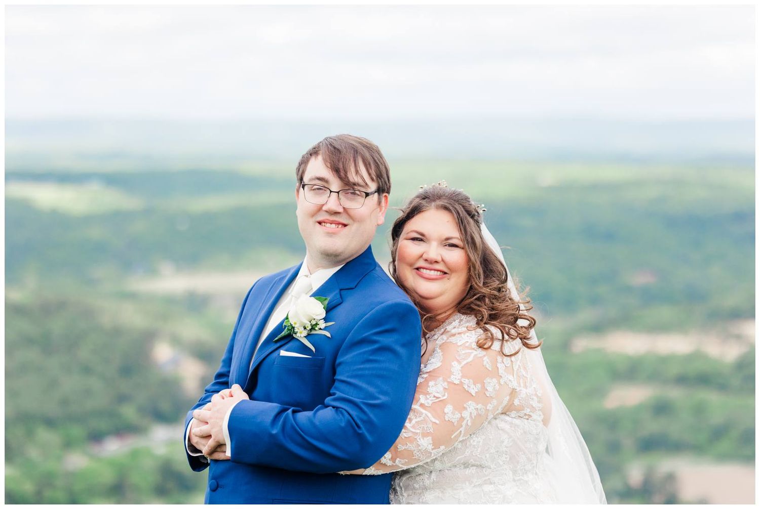 Happy newlyweds smile together on mountain overlook during their outdoor wedding.
