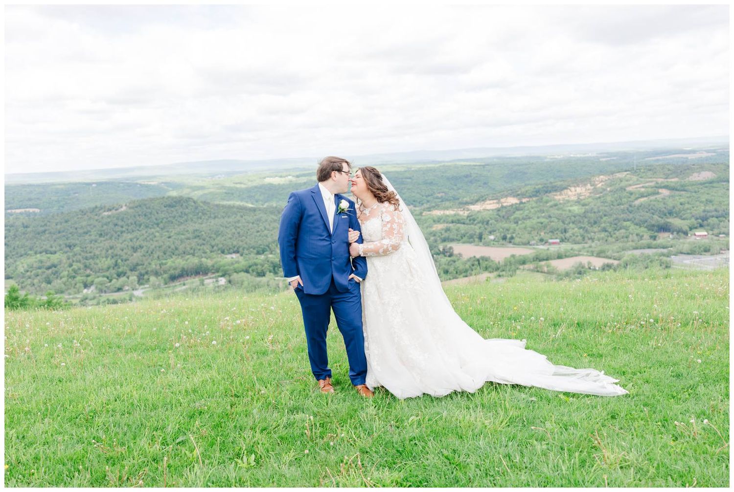 A couple shares a romantic moment on a hilltop overlooking a lush green valley landscape.