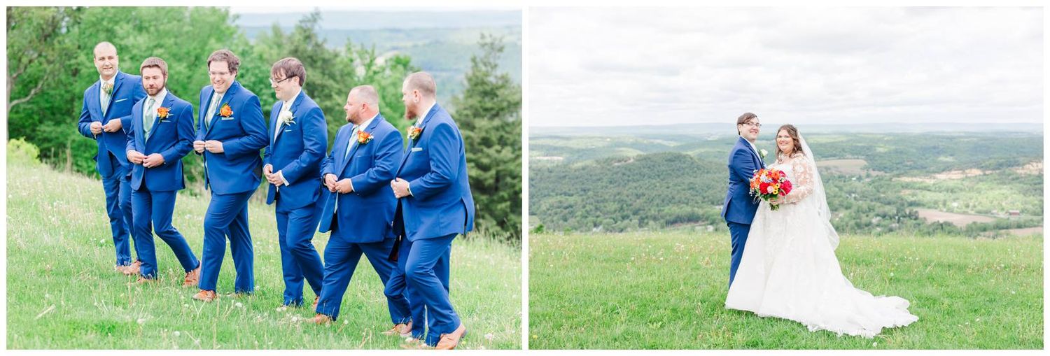 A group in bright blue attire stands playfully on a grassy hillside next to a couple sharing a romantic moment outdoors.