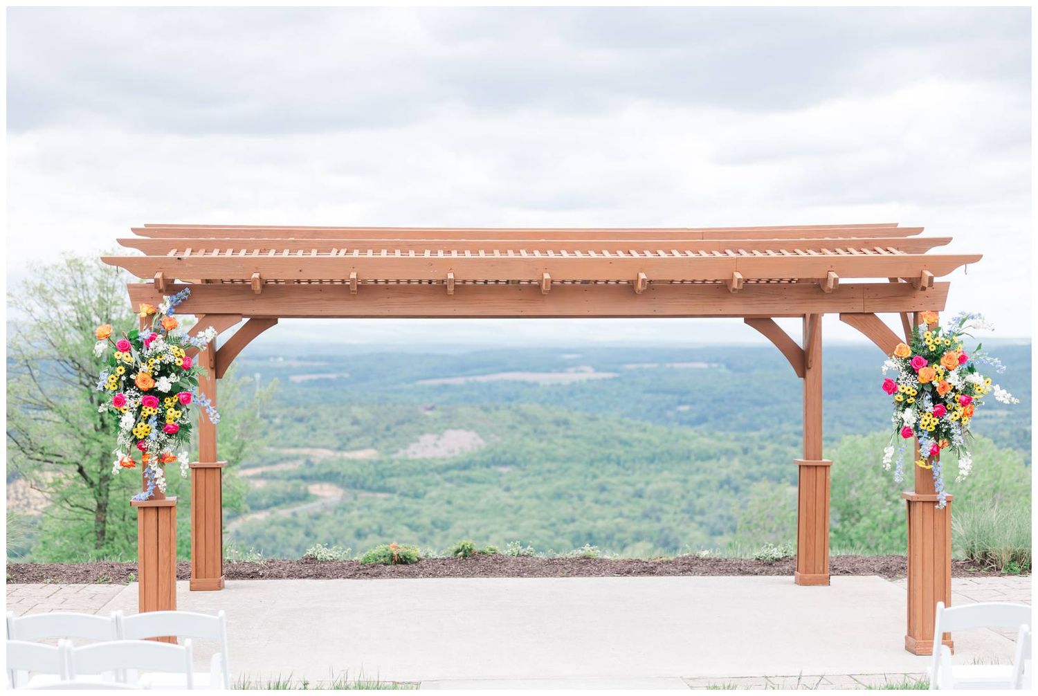 Wooden wedding arbor with floral arrangements overlooking a scenic mountain valley view.