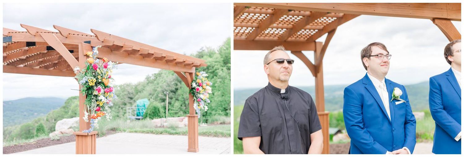 A wooden pergola decorated with pink and coral floral arrangements next to groom and groomsmen in blue suits at outdoor wedding.