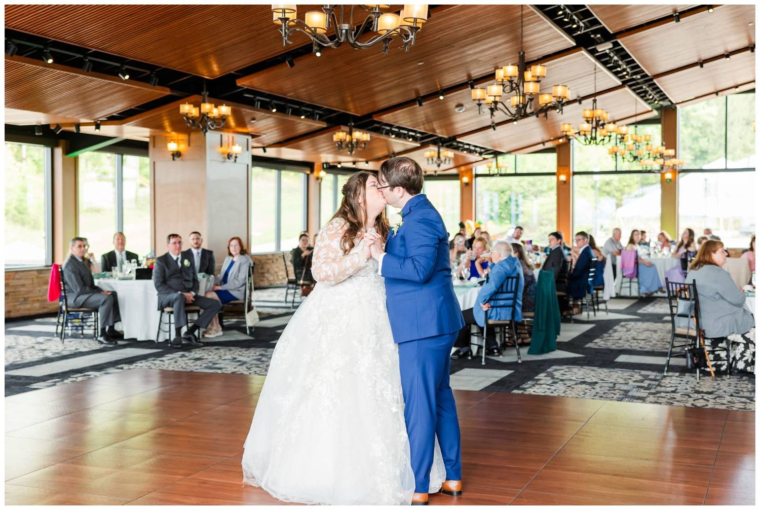 A couple shares their first dance at their wedding reception in a rustic venue with wooden beams and chandeliers.