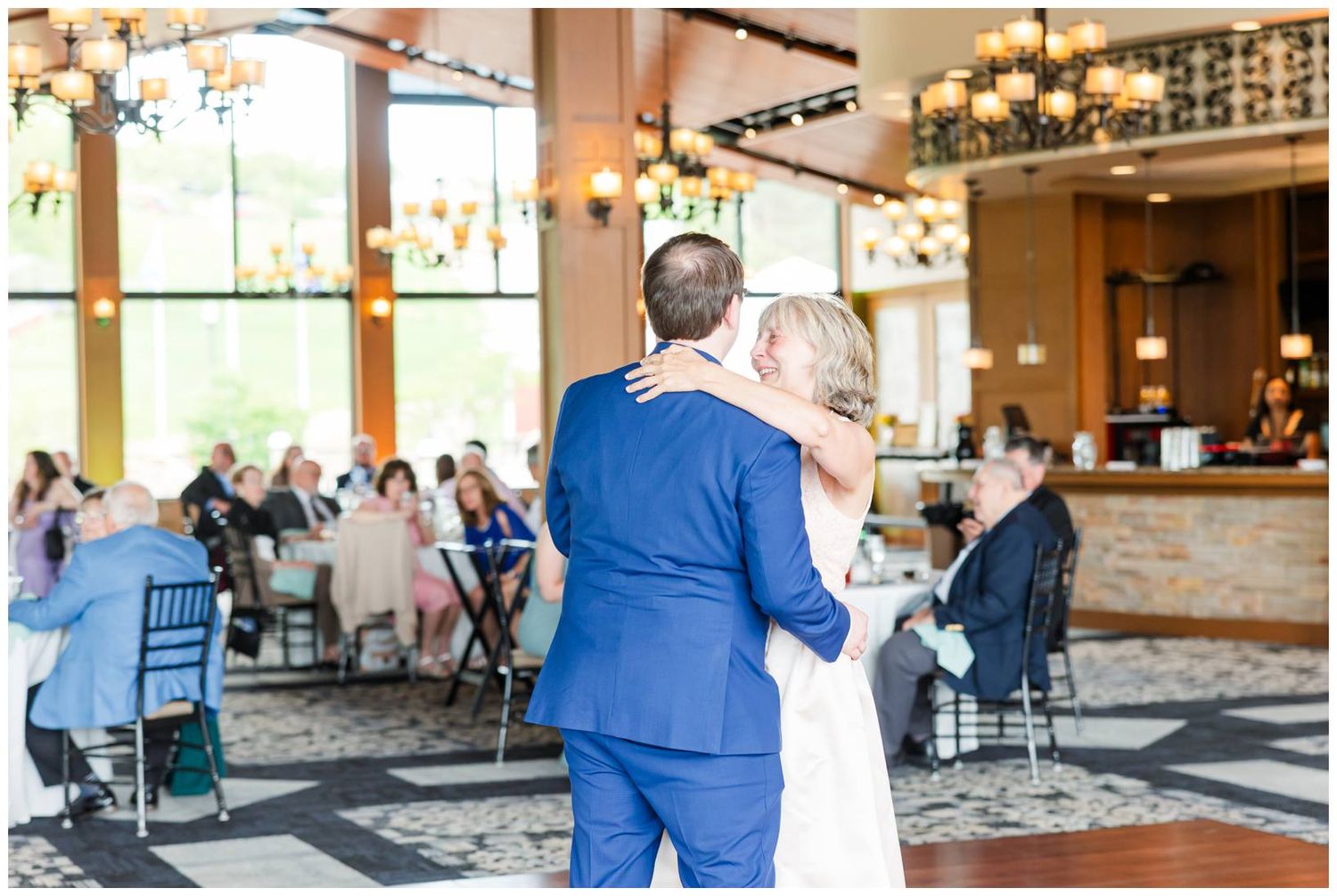 Couple shares a romantic dance in an elegant reception venue with guests seated at tables and a bar in the background.