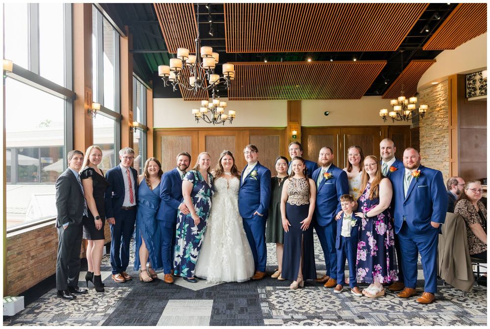 Wedding celebration group gathers in elegant venue with chandelier lighting and modern decor.