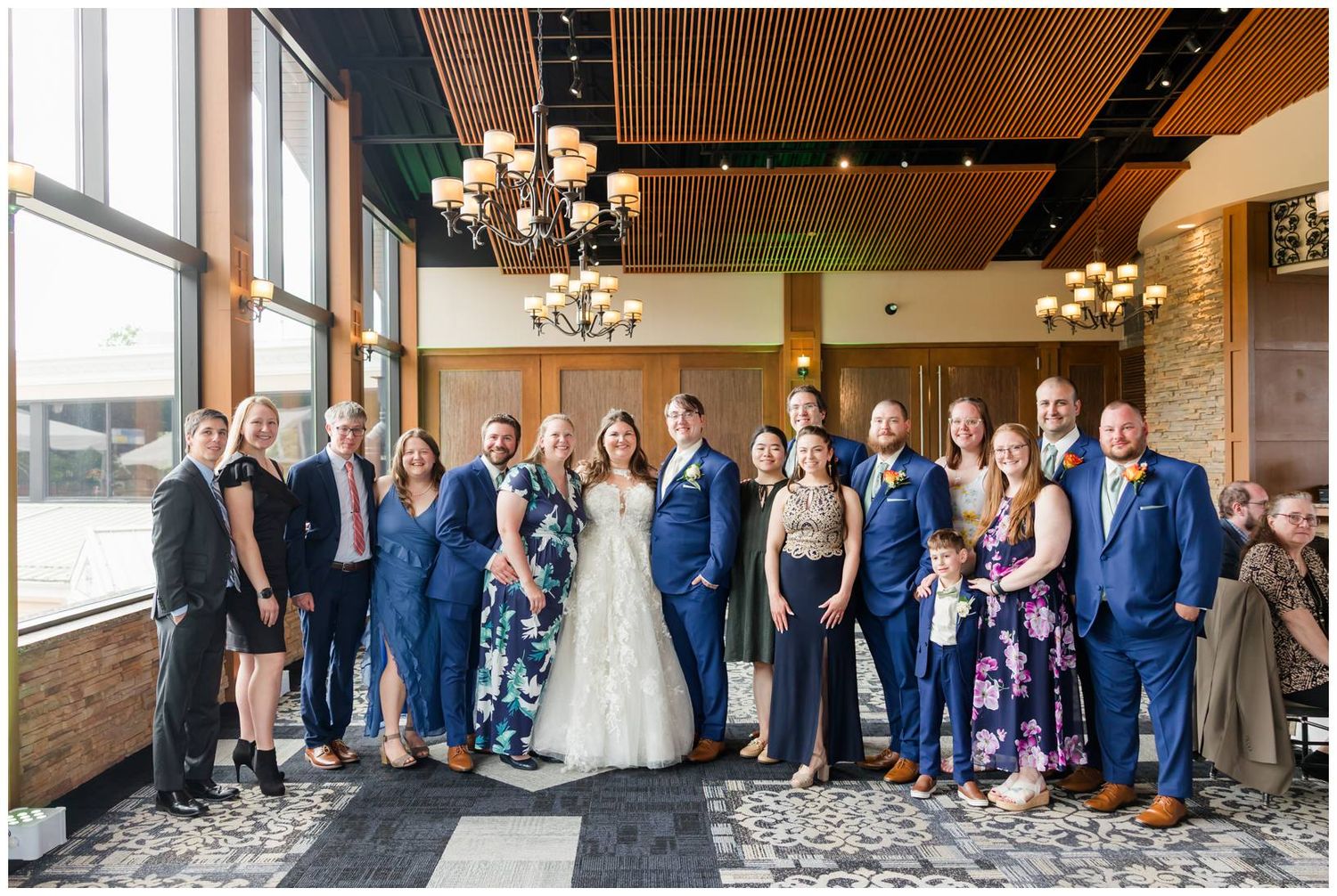 Wedding celebration group gathers in elegant venue with chandelier lighting and modern decor.