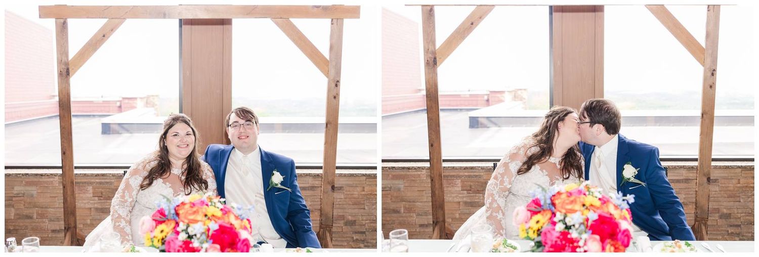 Couple shares romantic moments at rustic wood-beamed venue with vibrant pink and coral floral centerpiece on table.