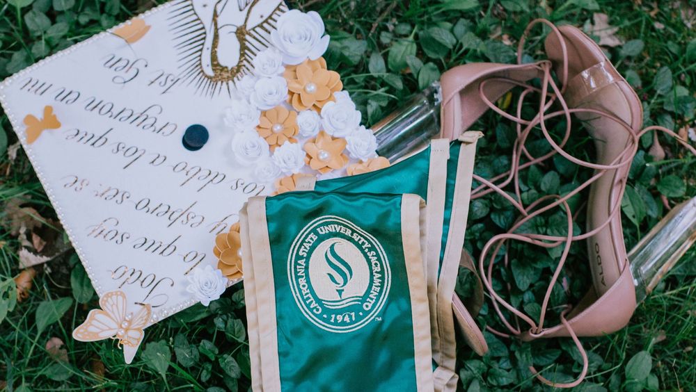 A decorative paper note with gold butterfly details lies on grass next to teal packaging and pink designer shoes.