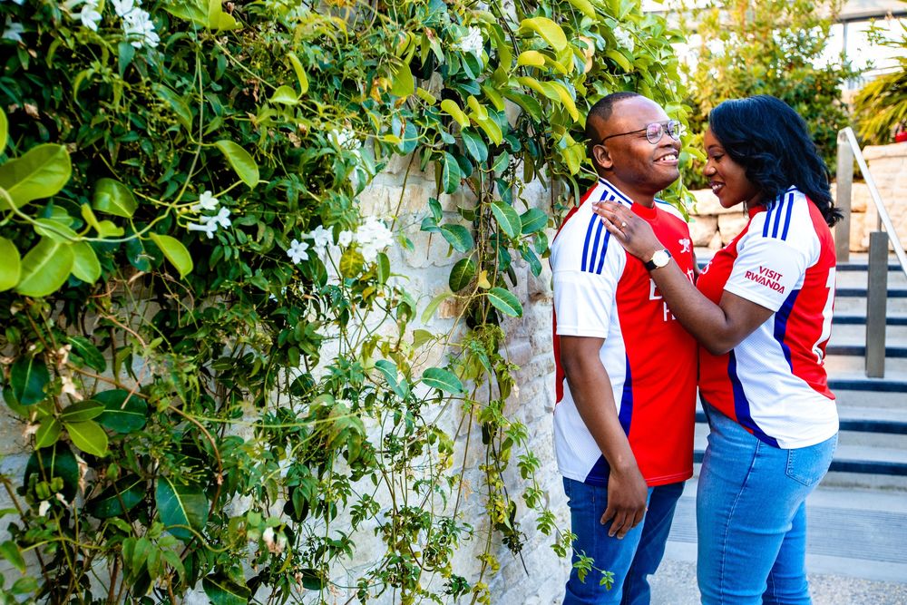 Couple in casual sports attire laugh and smile together while standing near lush green vines on outdoor stairway.