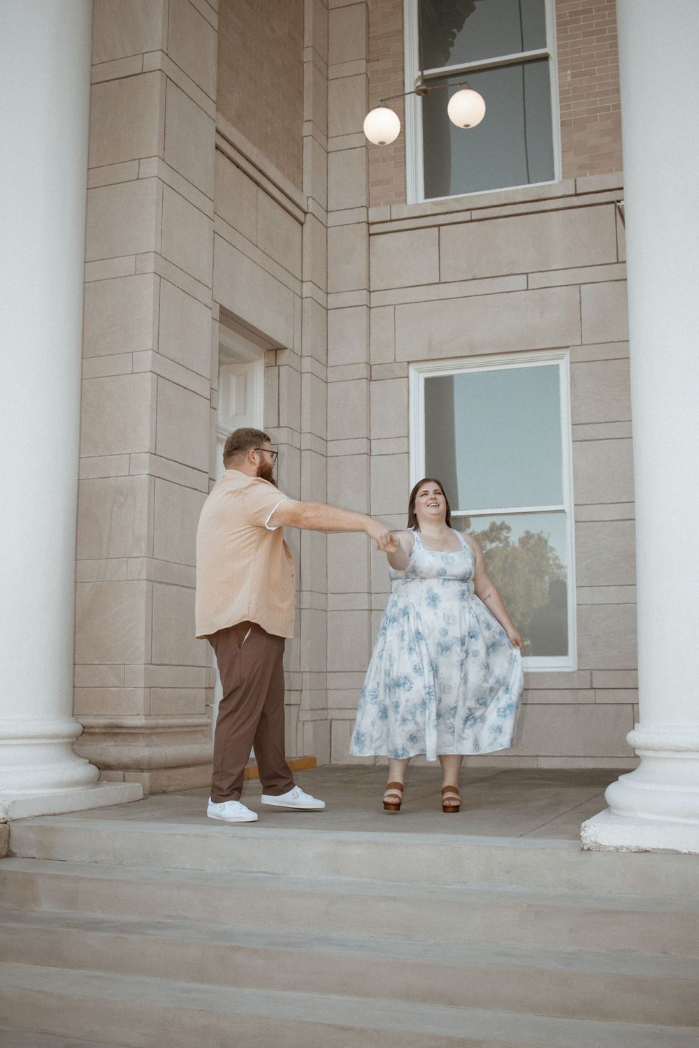 Couple holding hands on steps of elegant stone building with tall white columns.