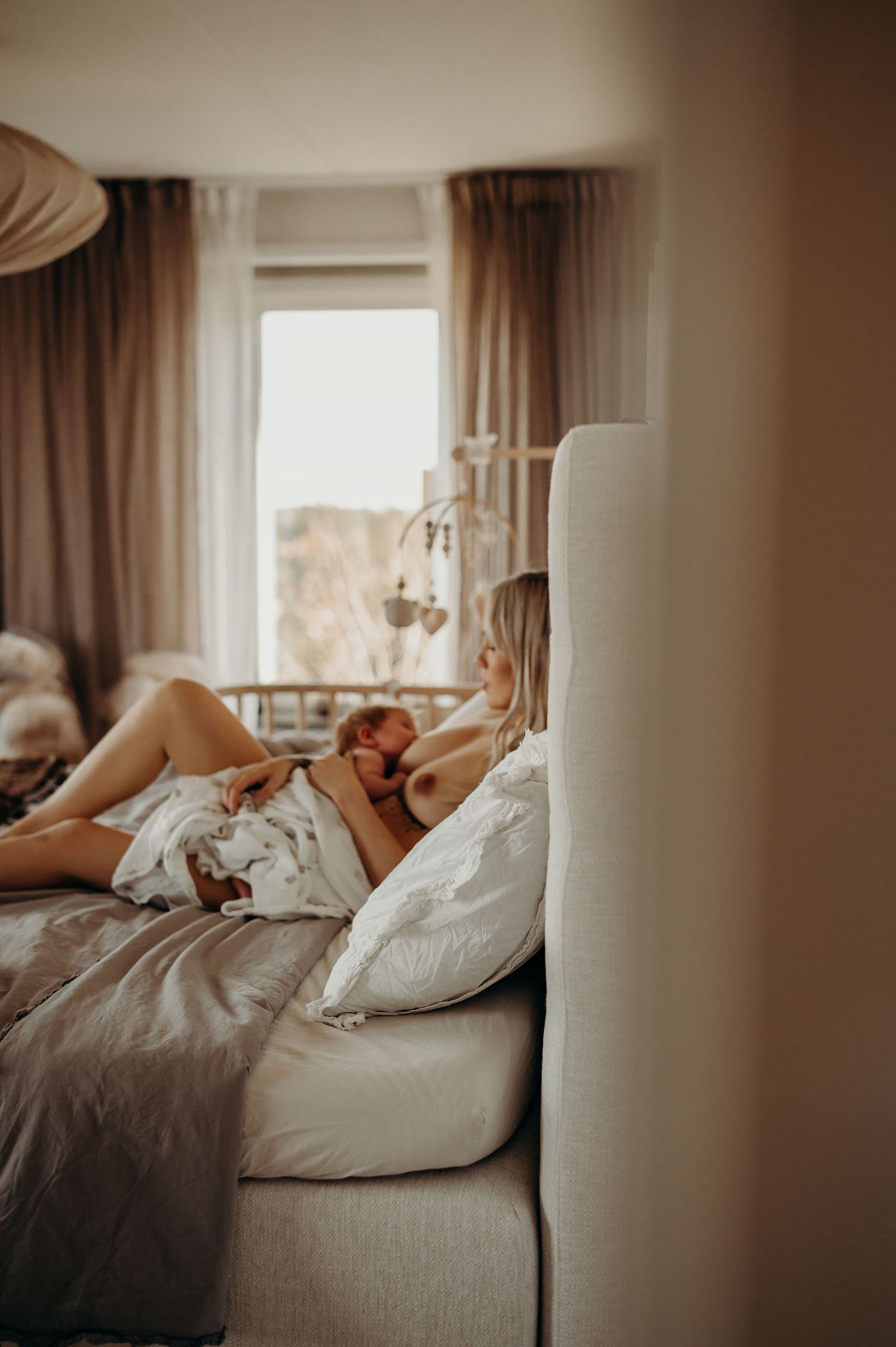 nyföddfotografering i hemmet, mamma som sitter i sängen och ammar sin son