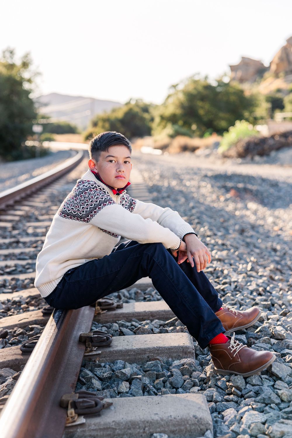Person sitting on train tracks wearing a white sweater with leopard print detail and brown boots at sunset.