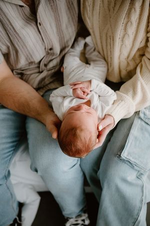 Two parents in cradling their newborn baby dressed in white, a tender family moment captured by newborn photographer Story & Soul Mandurah