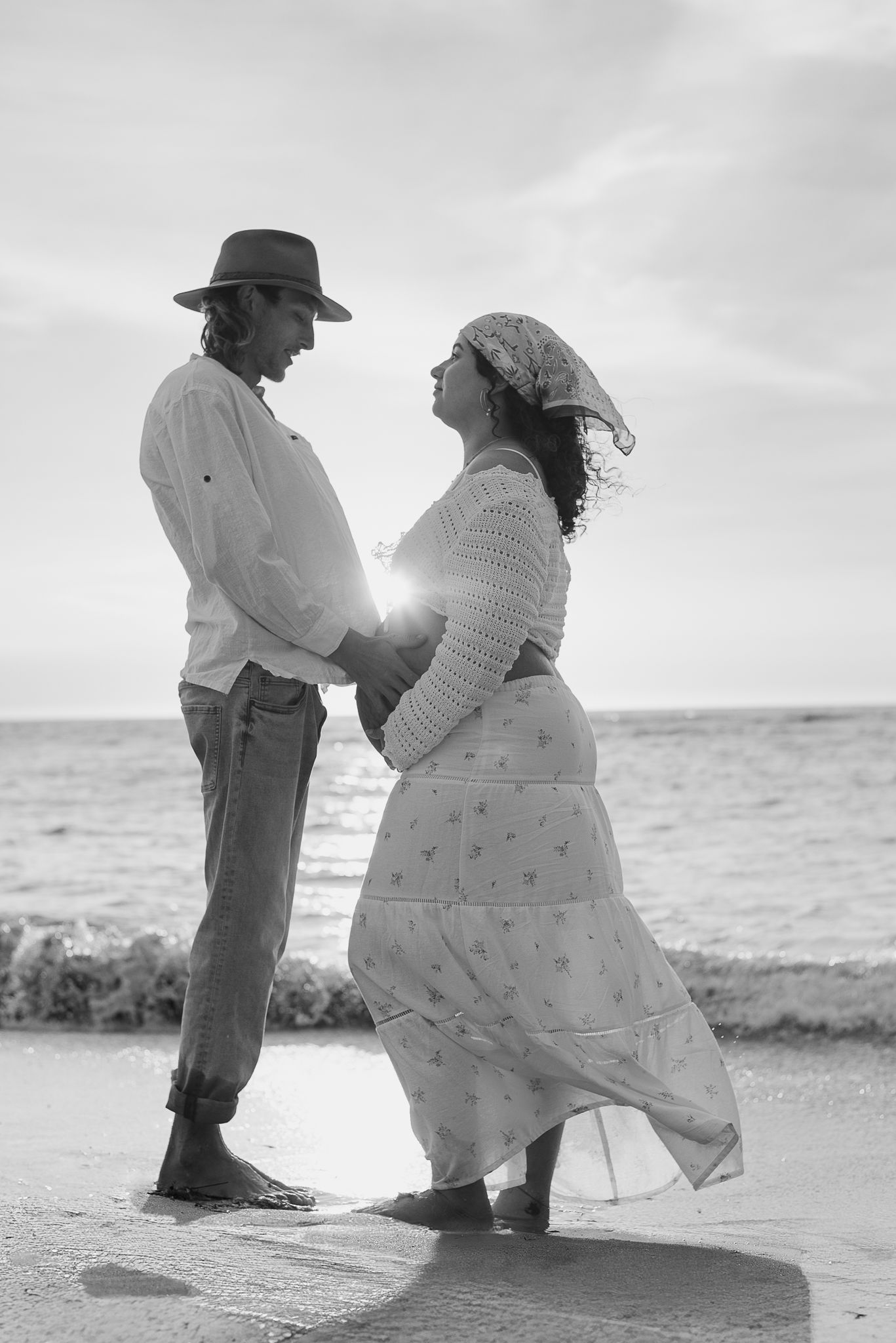 A romantic black and white photo photo showing a couple holding baby bump on a beach at sunset. Mandurah Maternity Photographer.
