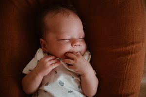 Peaceful newborn baby sleeping on a rust-colored chair, wearing a white onesie for newborn photographer story & soul photography Mandurah WA
