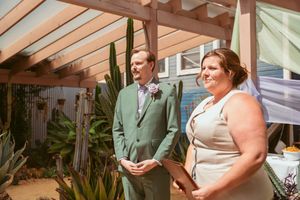 Wedding ceremony taking place in a greenhouse conservatory with rustic wooden beams and desert plants.