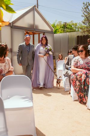 A wedding processional outdoors with white chairs and guests in attendance at a charming backyard venue.