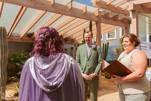 A small wedding ceremony takes place in a sunlit wooden pergola with houseplants surrounding the participants.