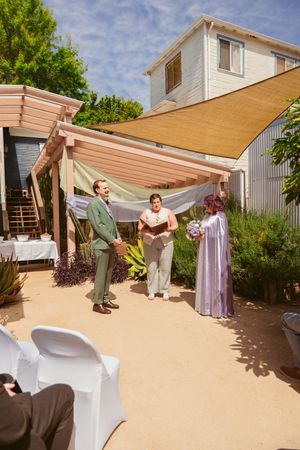 Outdoor wedding ceremony under a tan shade sail with desert-style landscaping and white chairs.