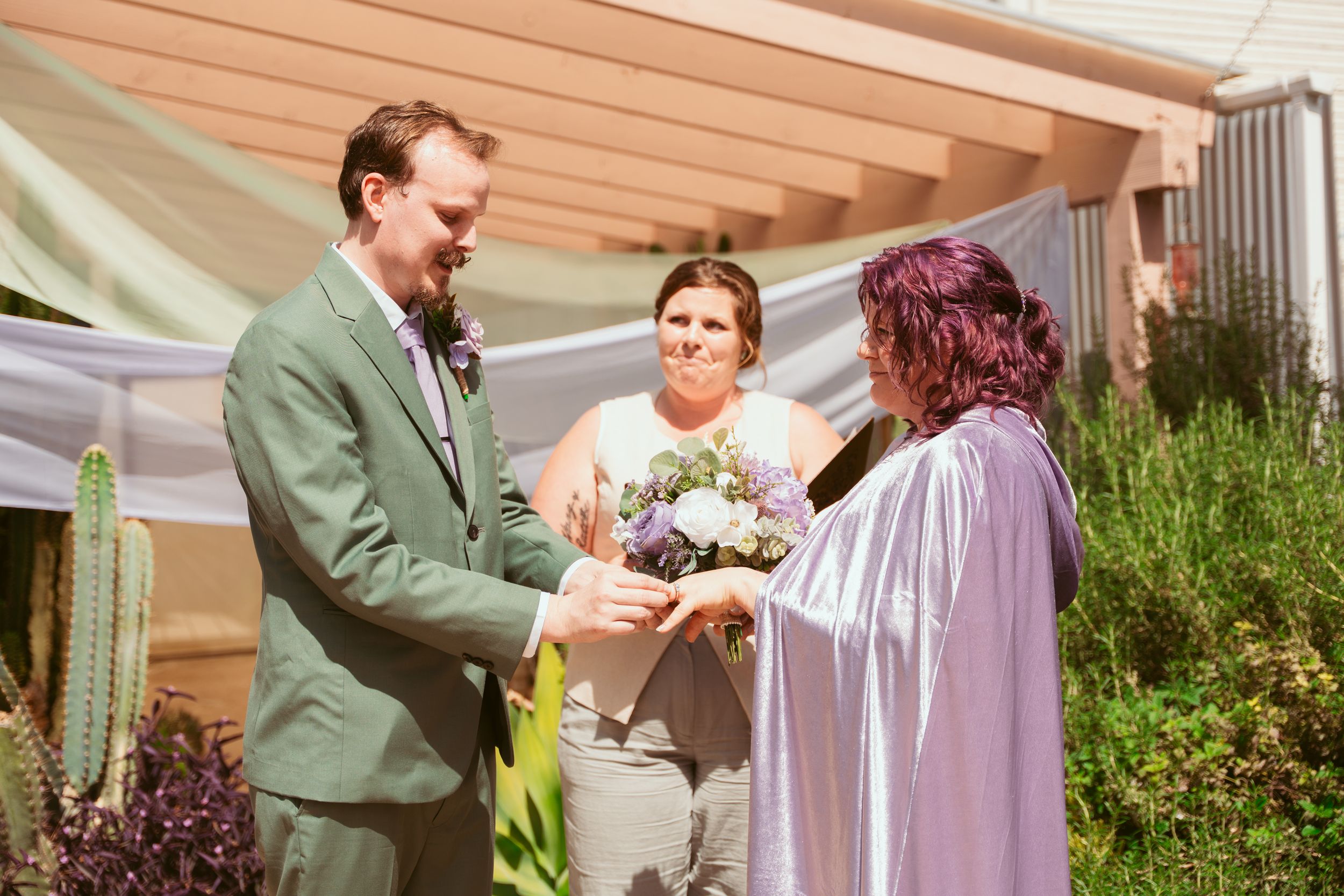 An outdoor wedding ceremony takes place on a porch with desert landscaping and cacti in the background.