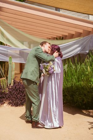 A romantic wedding moment between a couple under a draped canopy with pink beams and desert landscaping.