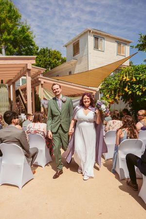 A joyful recessional at an outdoor wedding with white chairs and natural garden backdrop.