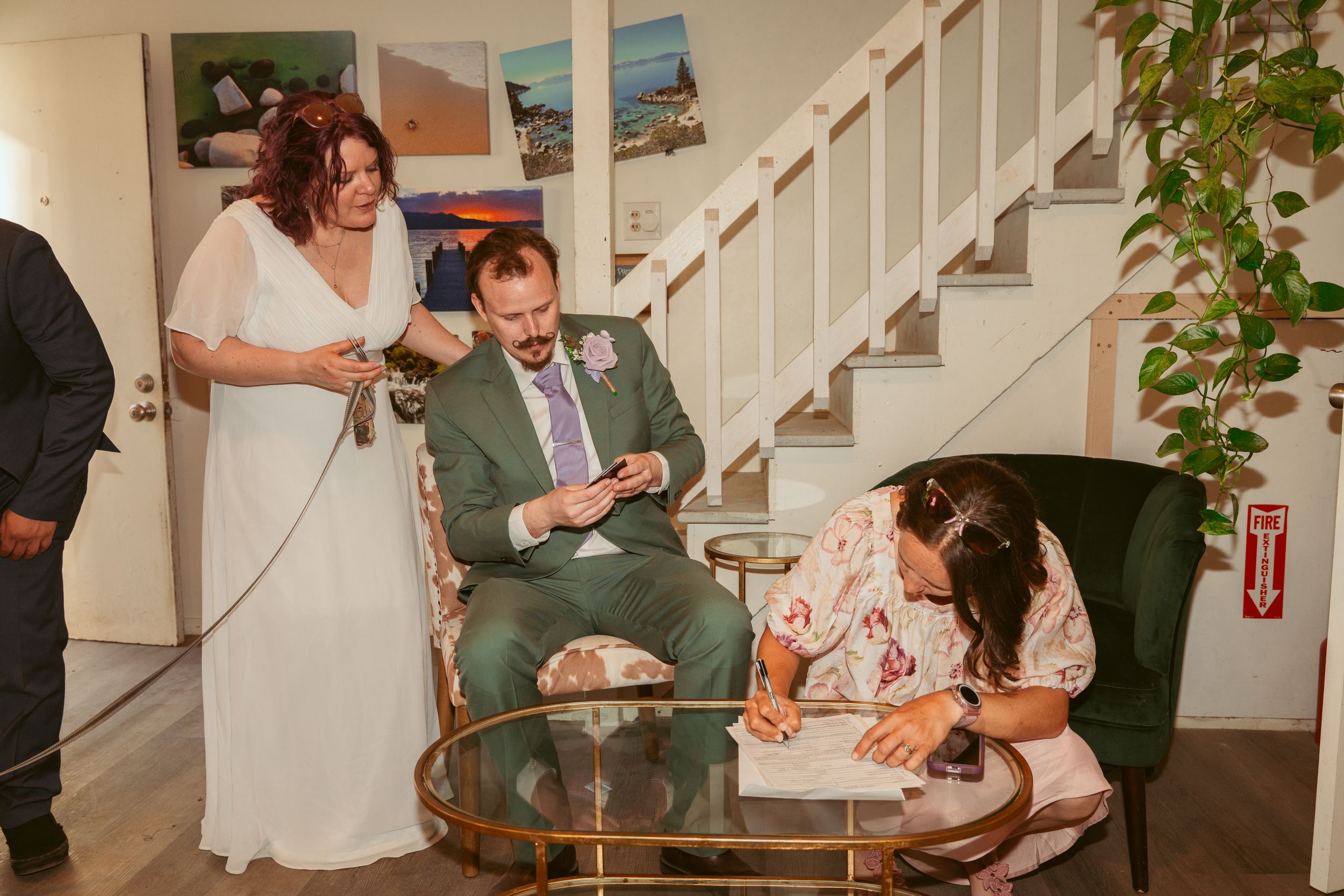 Informal wedding gathering showing people relaxing in a living room with stairs and green plants in the background.