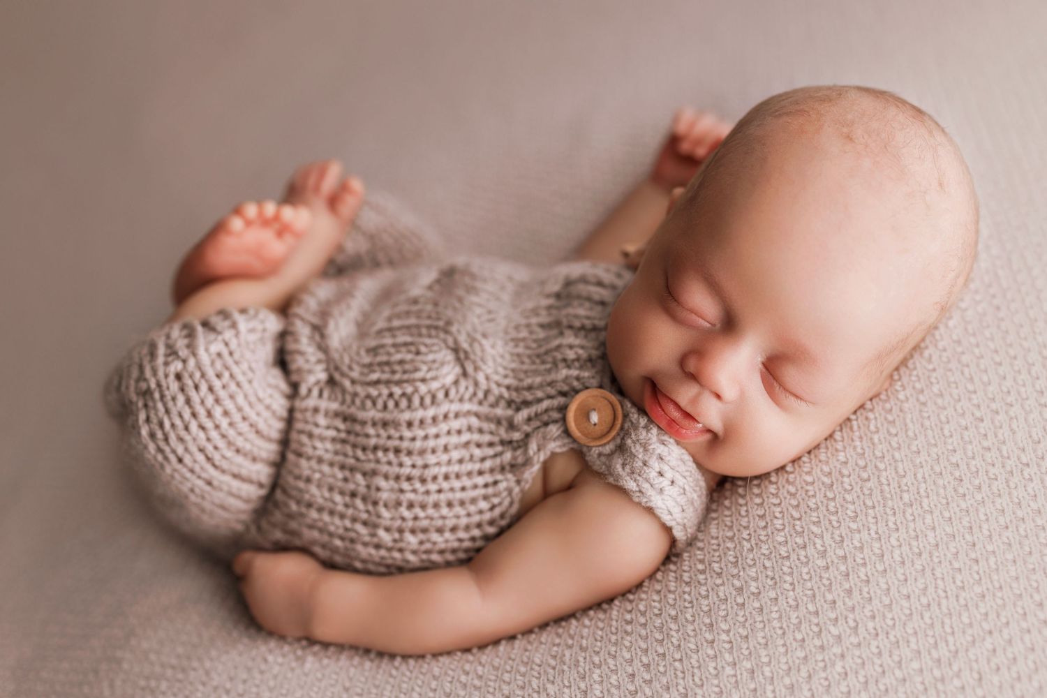 Sleeping baby wearing cozy knitted sweater with wooden button lies peacefully on soft beige fabric.