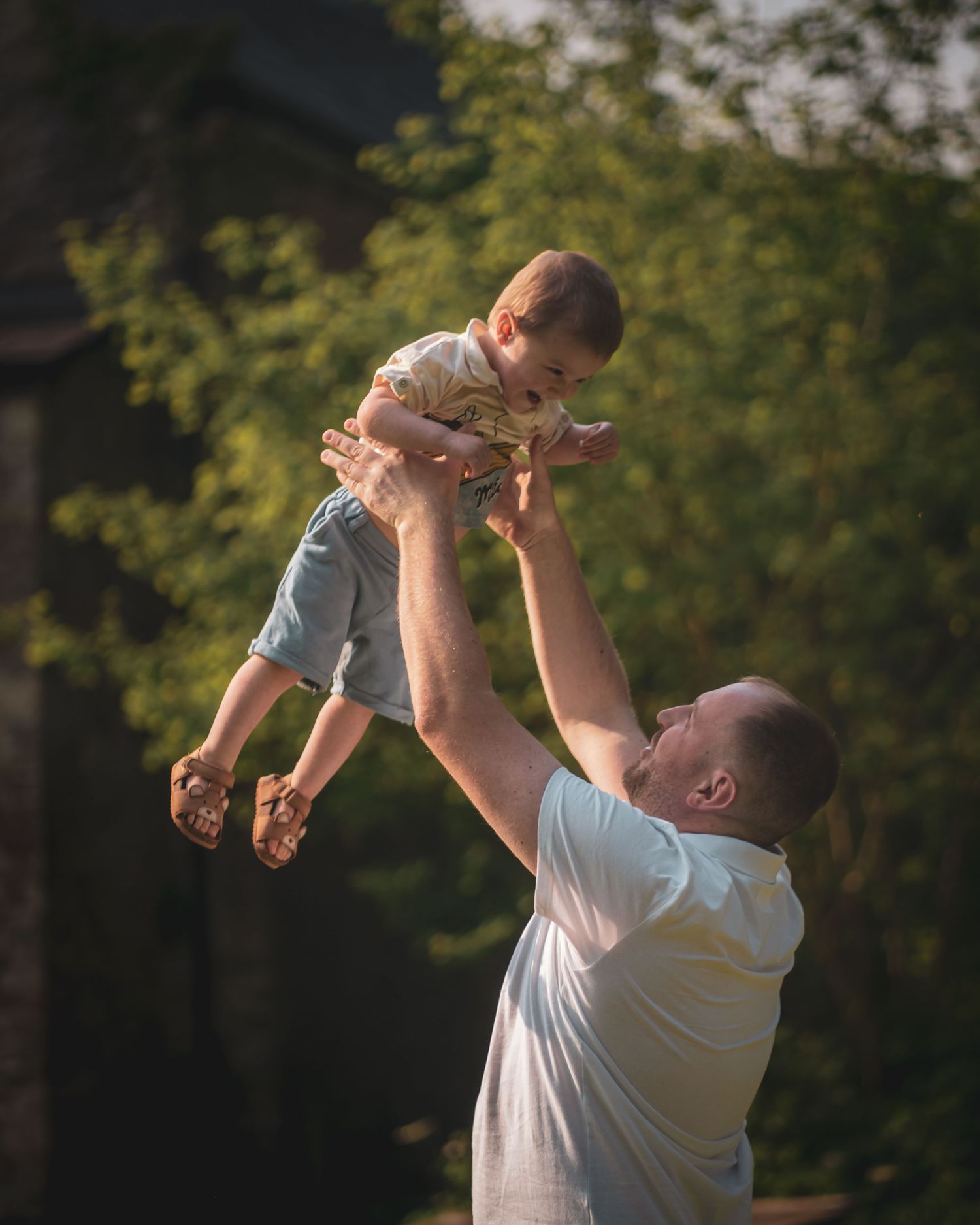 Parent lifts happy child into the air during a playful outdoor moment at sunset.