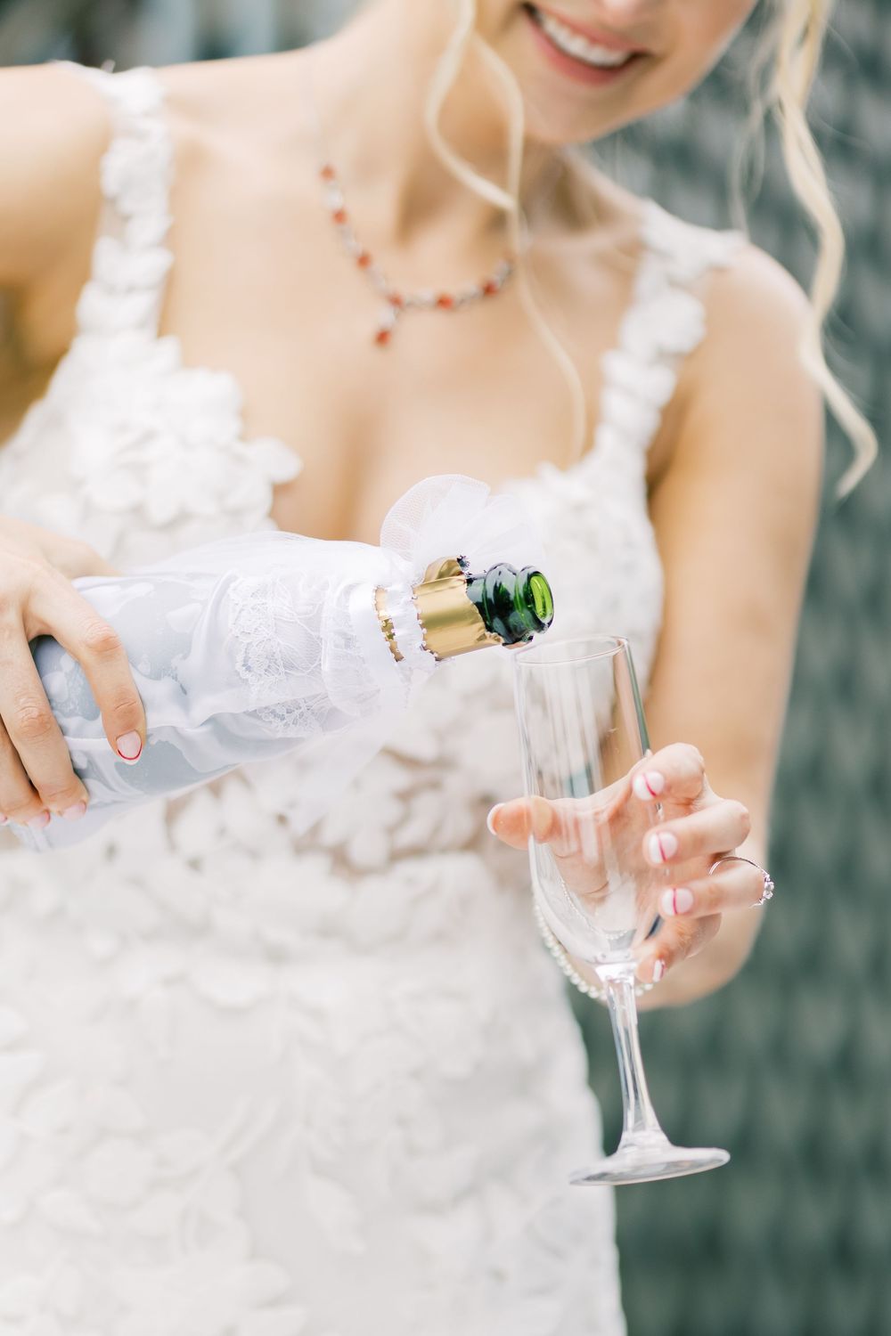 Bride in lace dress pouring champagne into a crystal glass during wedding celebration in Orange County, New York.