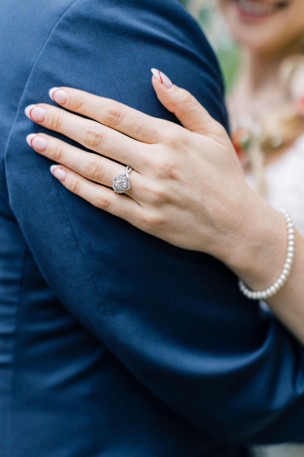 Close-up of a diamond engagement ring against a navy blue suit sleeve in Orange County, New York.