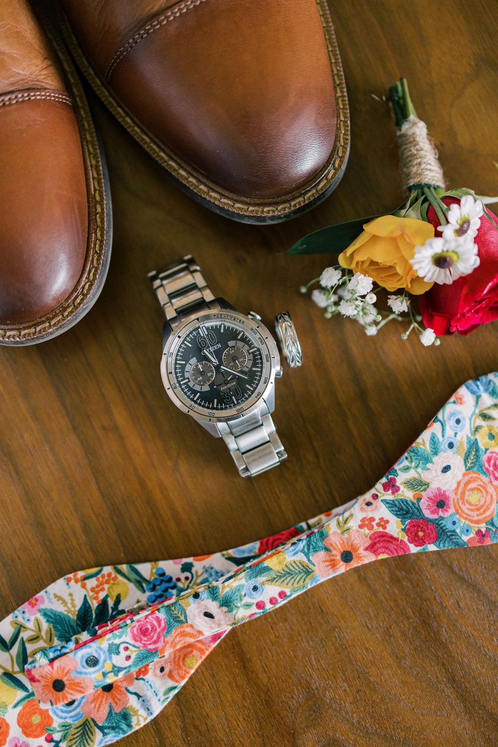 Brown leather dress shoes with watch and floral bow tie on wooden surface in Orange County, New York.