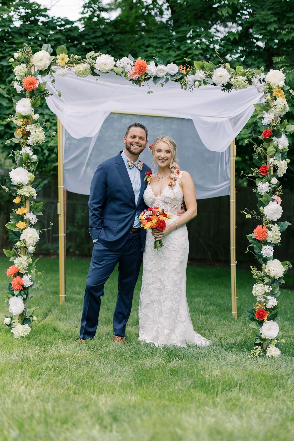 Wedding ceremony arch decorated with white and coral flowers against a green garden backdrop in Orange County, New York.