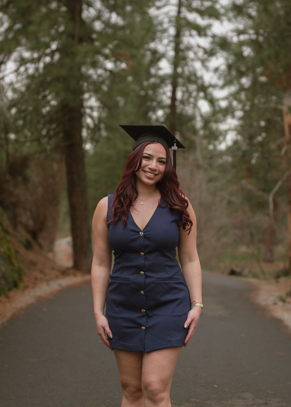 College graduate in navy blue dress smiling excitedly with hands placed at side.