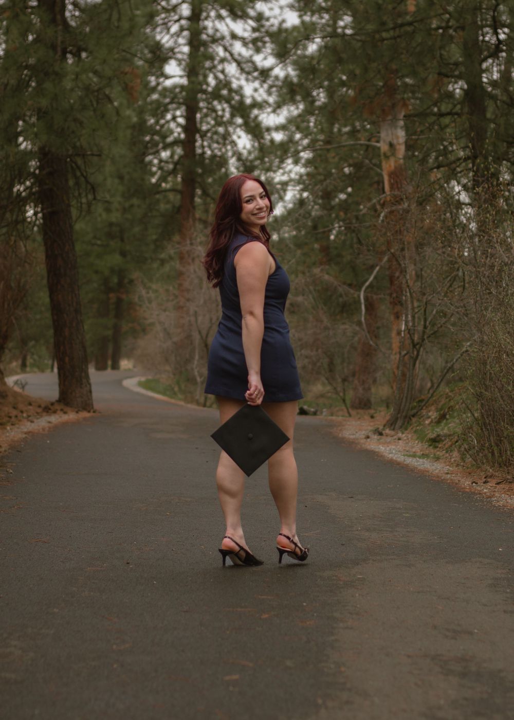 Redheaded woman looking back, holdin black graduation cap for GU Class of 2025.