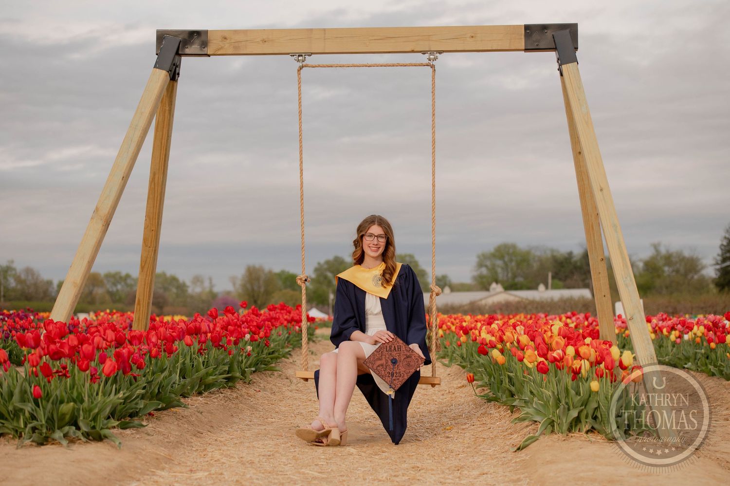 A rustic wooden swing set stands amidst vibrant red and orange tulip fields at sunset.
