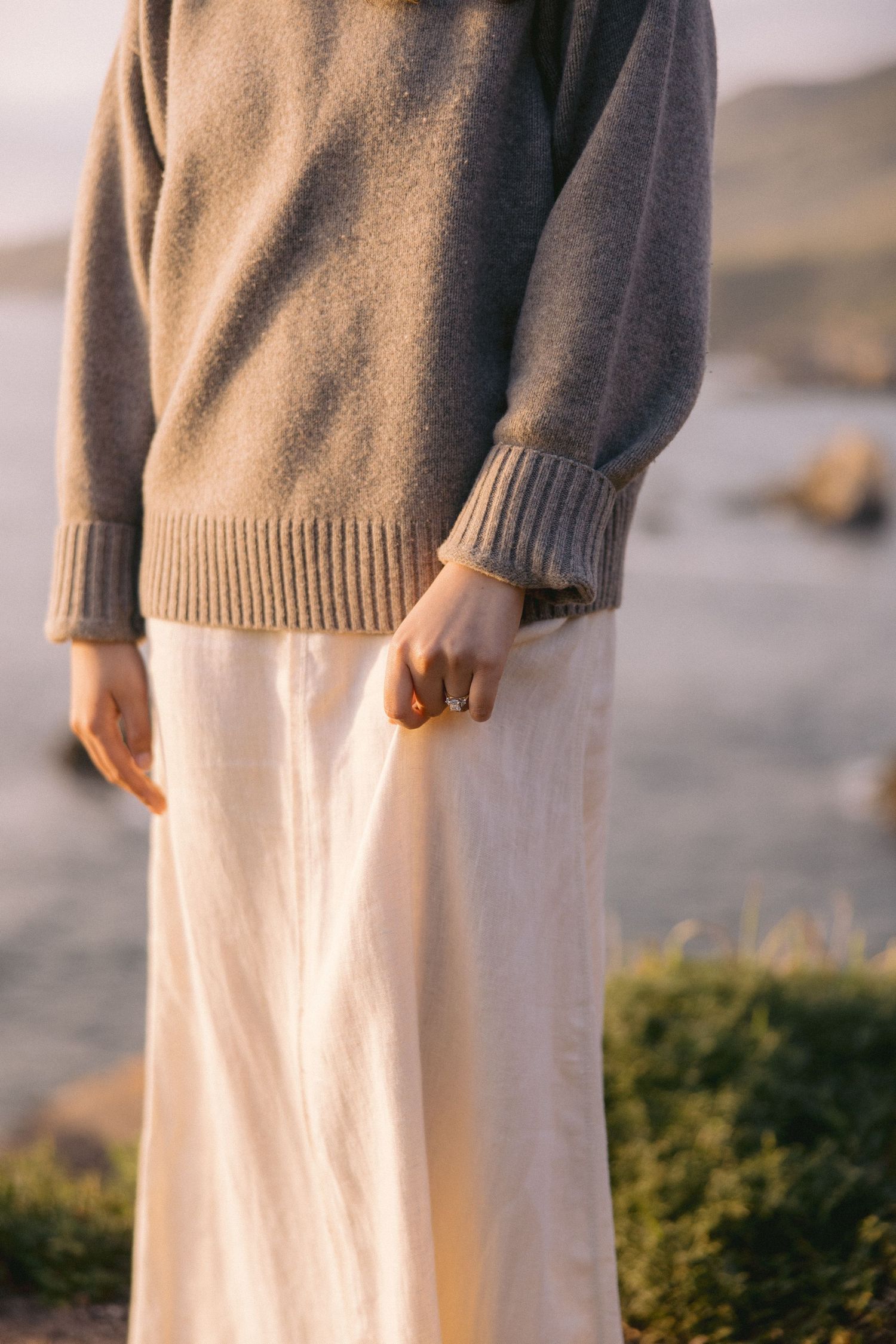 Person wearing a cozy brown knit sweater and flowy cream maxi skirt stands against soft outdoor lighting.
