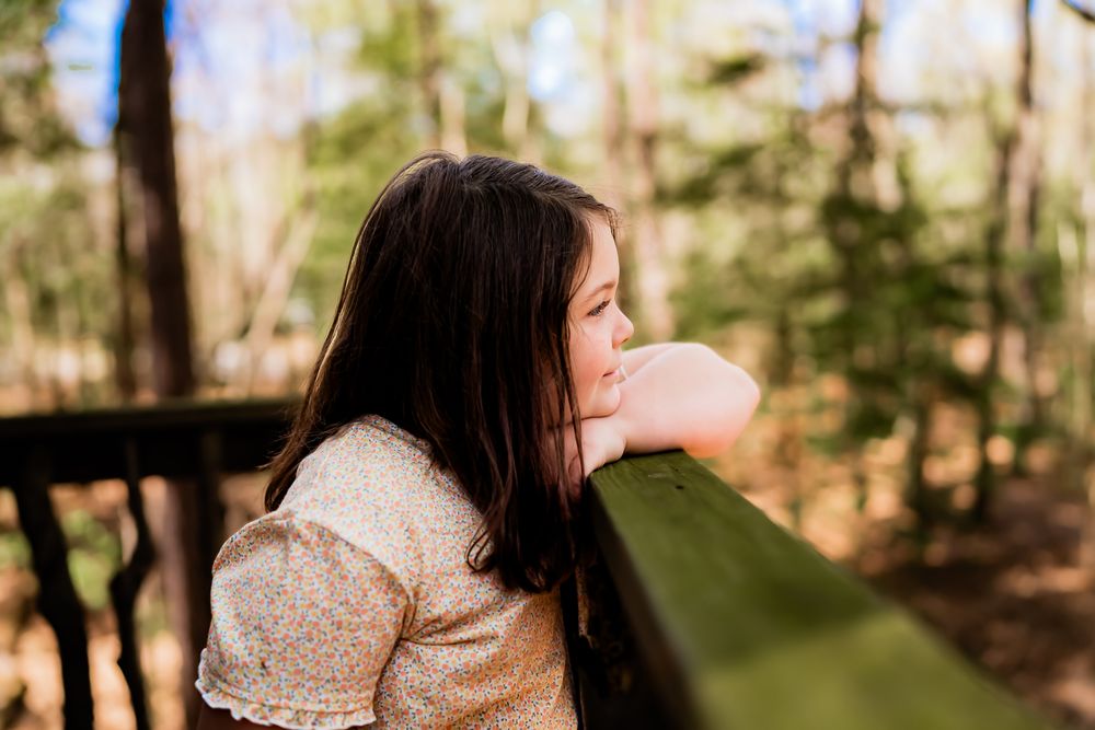 Side view of person in shimmery top leaning on green railing in wooded outdoor setting during daytime.