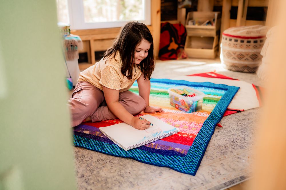 Someone lies on a colorful patterned blanket reading a book in a cozy home setting.