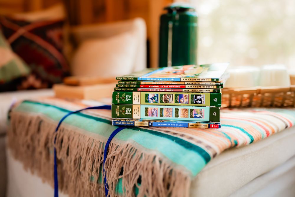 Vintage books and green beverage can resting on striped blanket with fringe tassels.