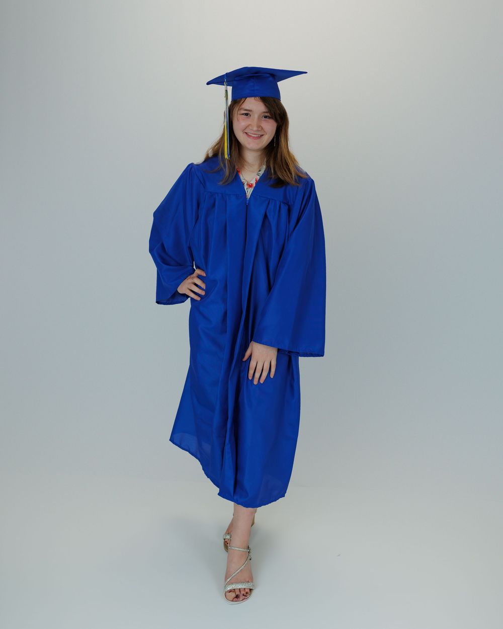 Graduate wearing royal blue cap and gown poses against light background for commencement portraits.
