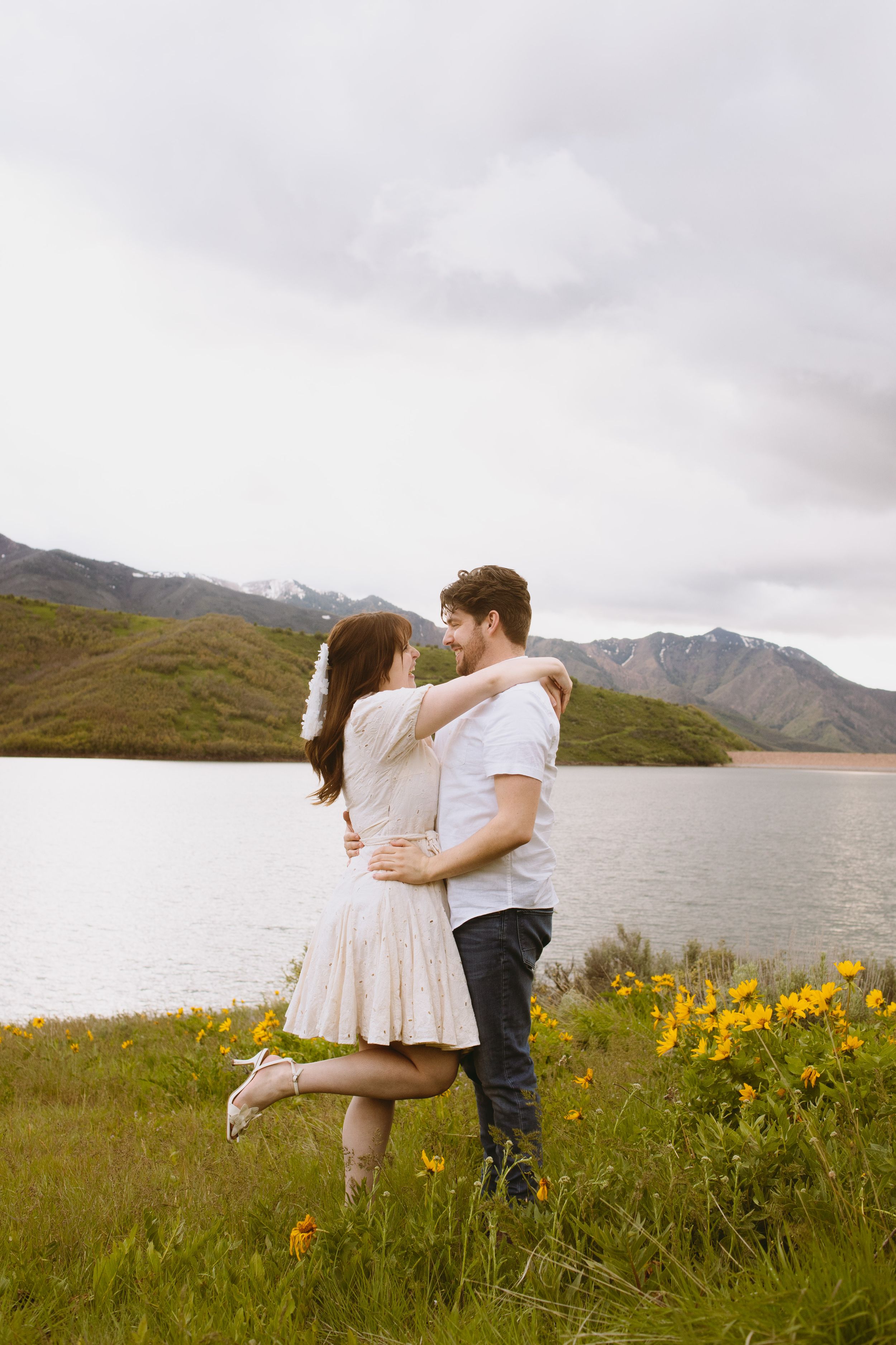 Embracing by a mountain lake with yellow wildflowers blooming in Salt Lake City, Utah.