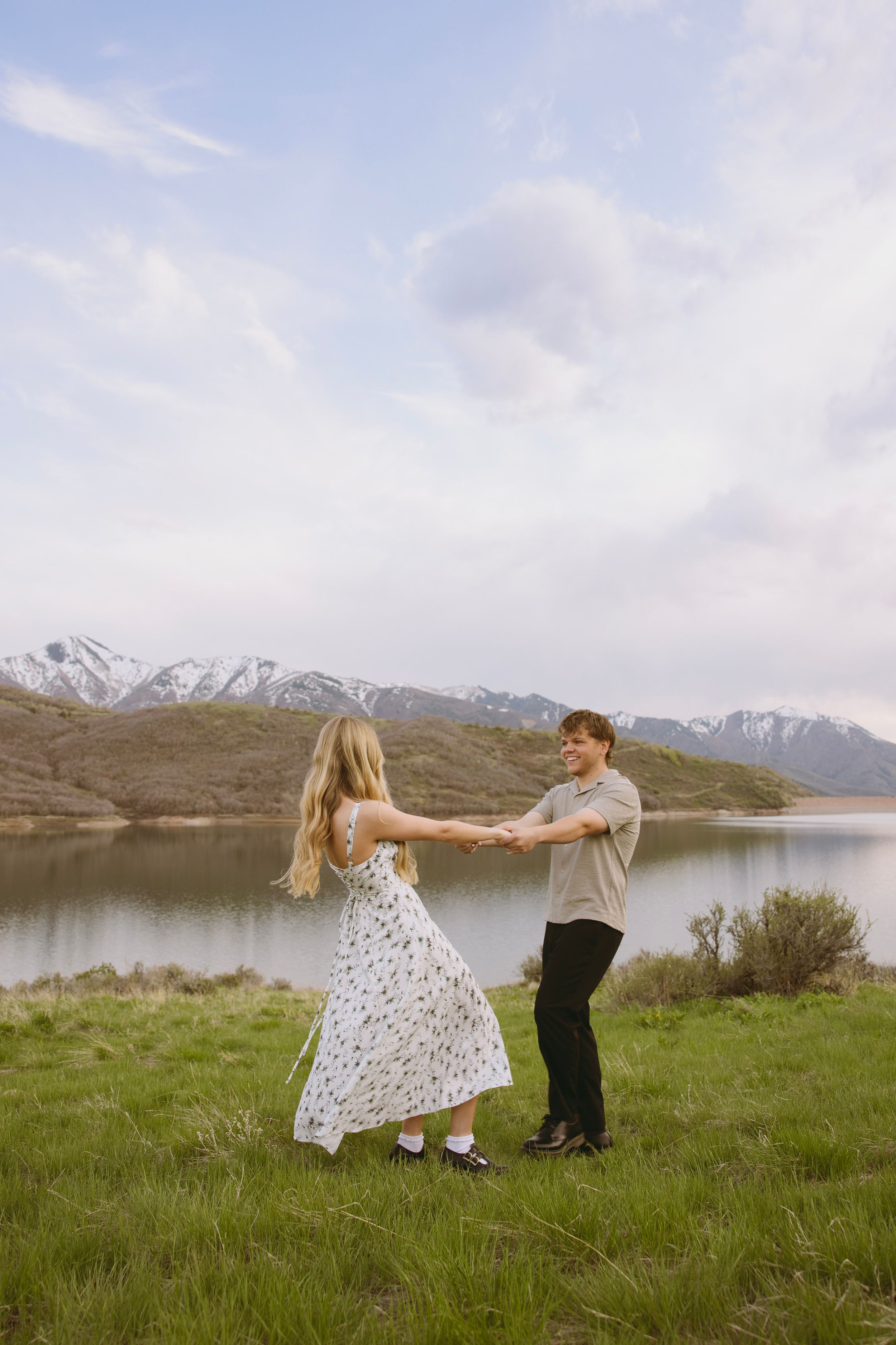 An engaged couple dancing in a floral dress against a backdrop of mountains and lake in Salt Lake City, Utah.