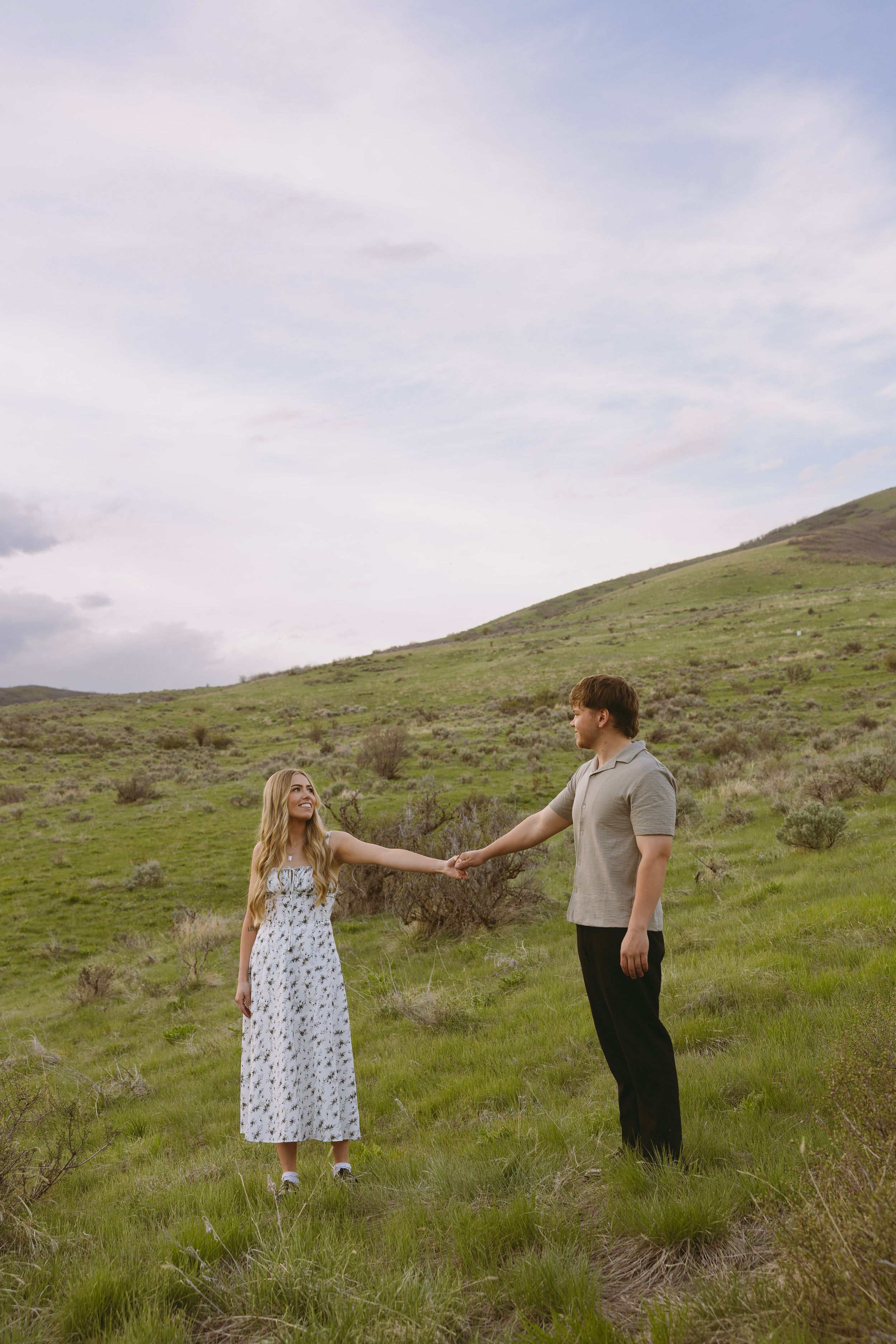 An engaged couple dancing together on a green hillside with mountains in the distance in Salt Lake City, Utah.