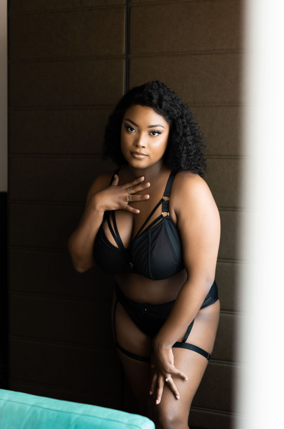 A woman in black lingerie poses confidently against a brown wall next to a turquoise pool.